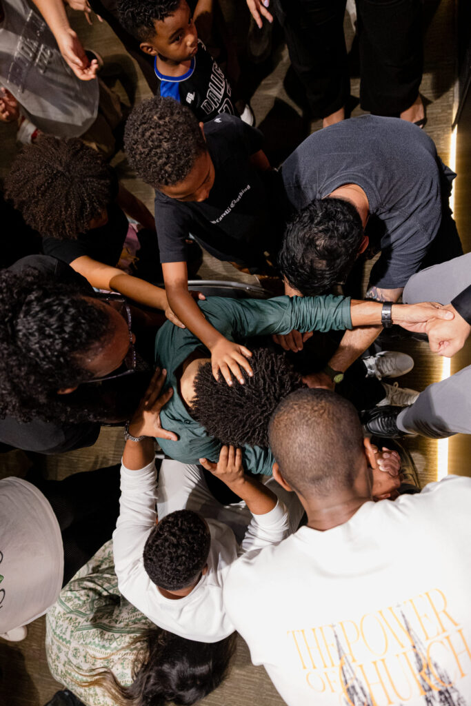 Pessoas reunidas em oração, com as mãos apoiadas sobre um participante.