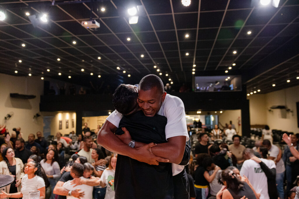 Dois homens se abraçam diante da comunidade reunida na igreja.
