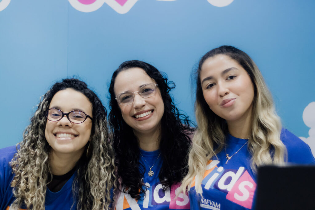 Três participantes com camisetas azuis do Kids diante de um painel azul.