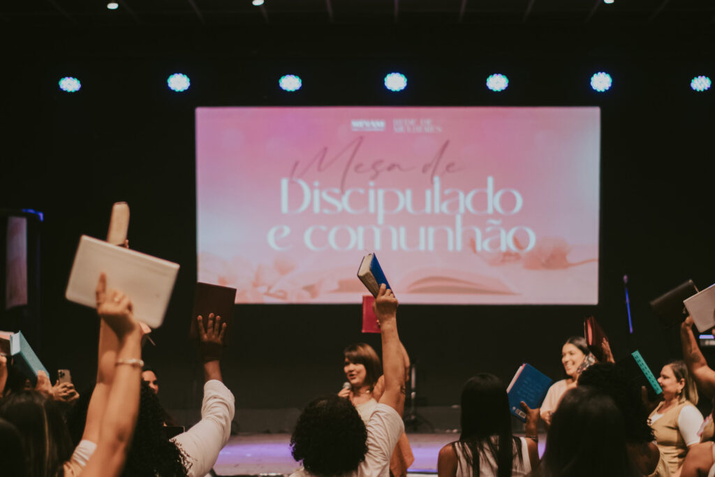 Pessoas reunidas na igreja seguram Bíblias durante momento de comunhão e louvor